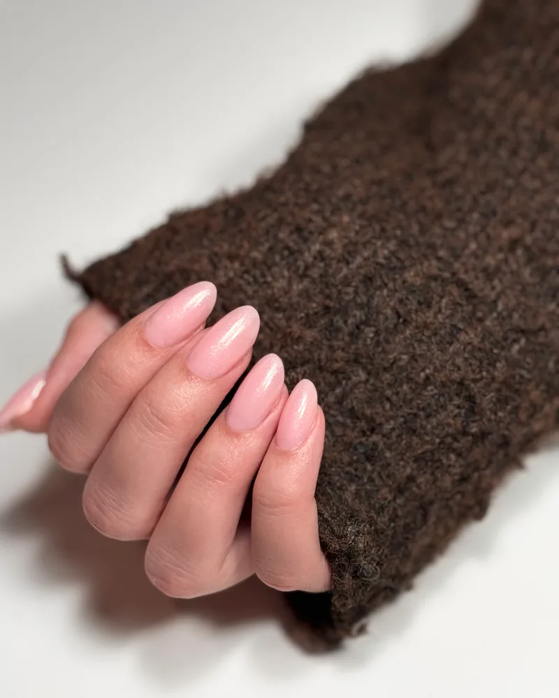 Pose gel rose nacré sur ongles amande, main posée sur une maille brune