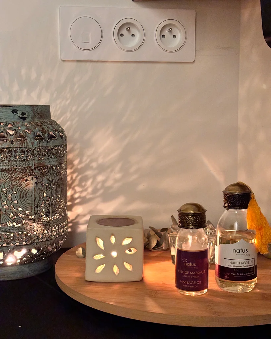 Les huiles de massage et le brûle-parfum de l'atelier, posés sur un plateau de bois dans la lumière chaude d'une lanterne
