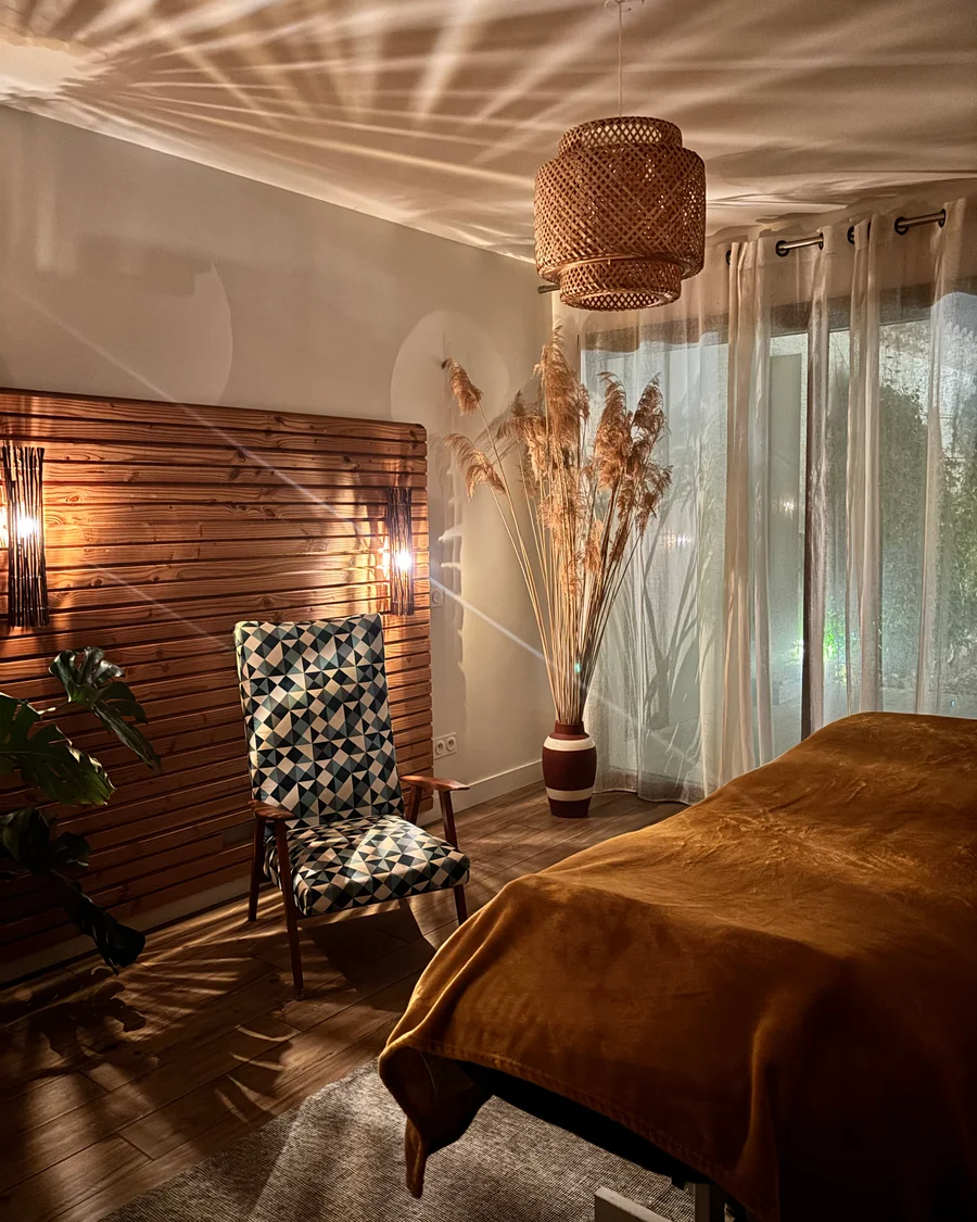La pièce dédiée aux massages : la table, le fauteuil et les herbes de la pampa devant le voilage